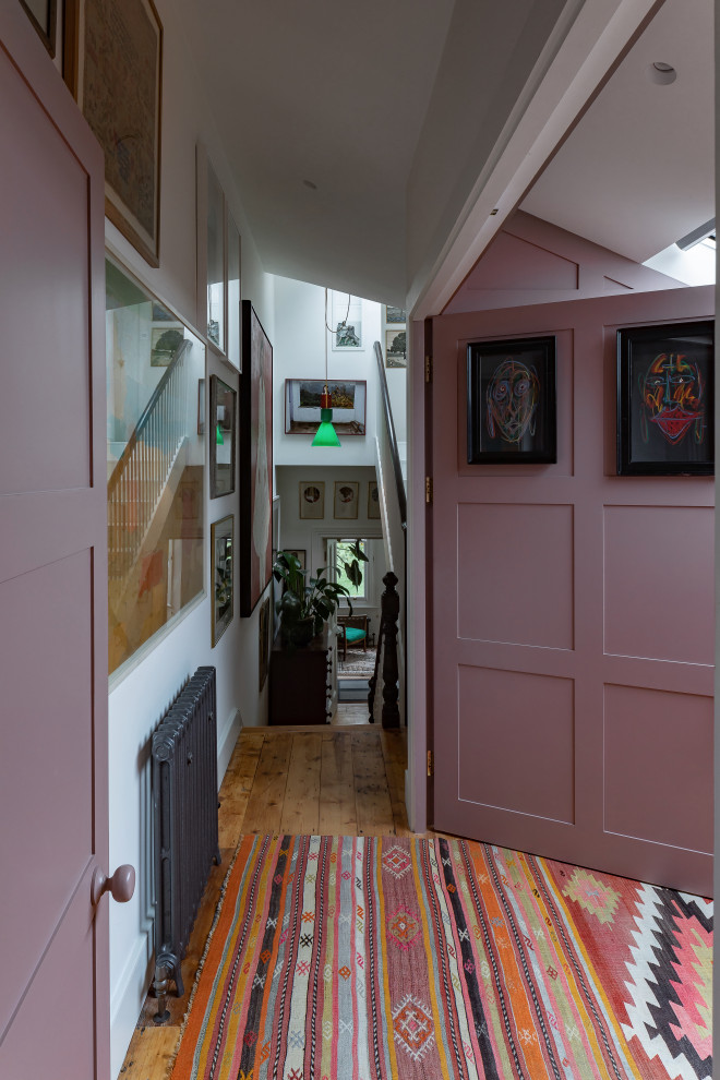 Photo of a mid-sized eclectic open concept living room in London with a library, pink walls, medium hardwood floors, a concealed tv and panelled walls.