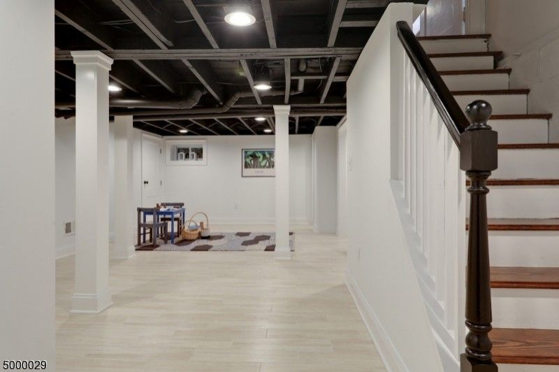 Photo of a transitional fully buried basement in New York with white walls, vinyl floors, beige floor and exposed beam.