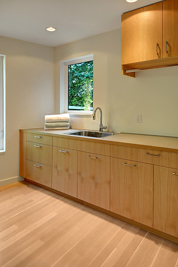 This is an example of a modern dedicated laundry room in Seattle with a drop-in sink, flat-panel cabinets, medium wood cabinets, white walls, light hardwood floors and a side-by-side washer and dryer.
