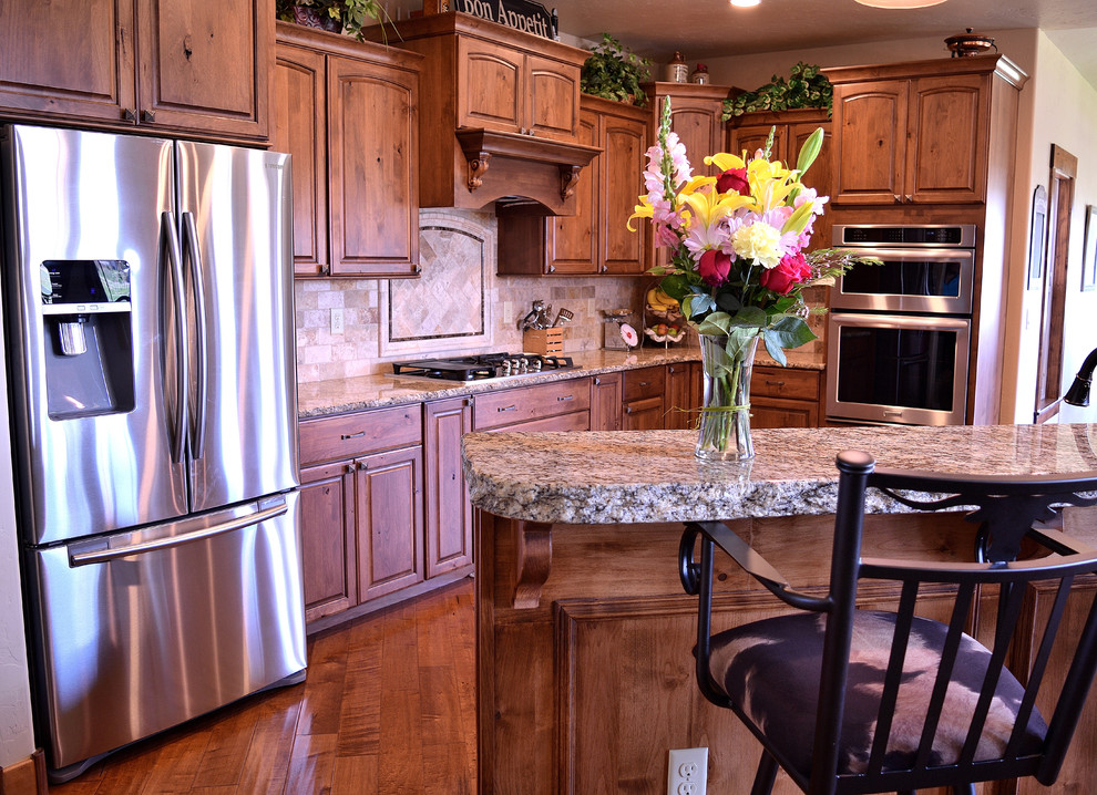 Inspiration for a large rustic galley medium tone wood floor and brown floor eat-in kitchen remodel in Denver with an undermount sink, raised-panel cabinets, medium tone wood cabinets, granite countertops, beige backsplash, stone tile backsplash, stainless steel appliances and an island