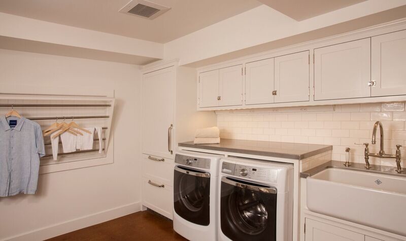 This is an example of a traditional laundry room in Seattle with a farmhouse sink, white cabinets, zinc benchtops, concrete floors and a side-by-side washer and dryer.