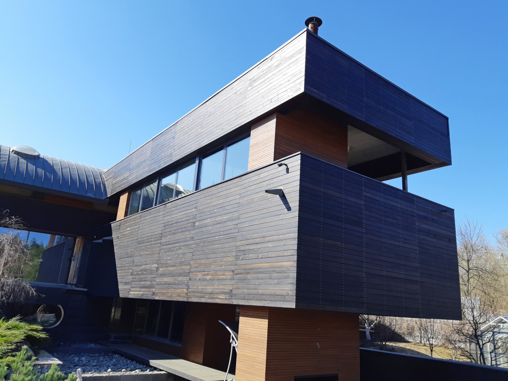 На фото: большой, деревянный, черный дом в современном стиле с разными уровнями, металлической крышей, серой крышей и отделкой планкеном