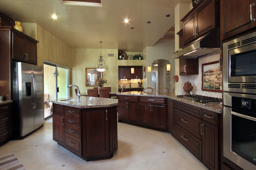 Inspiration for a large transitional concrete floor kitchen pantry remodel in Phoenix with an undermount sink, dark wood cabinets, granite countertops, beige backsplash, stone tile backsplash, stainless steel appliances, an island and raised-panel cabinets