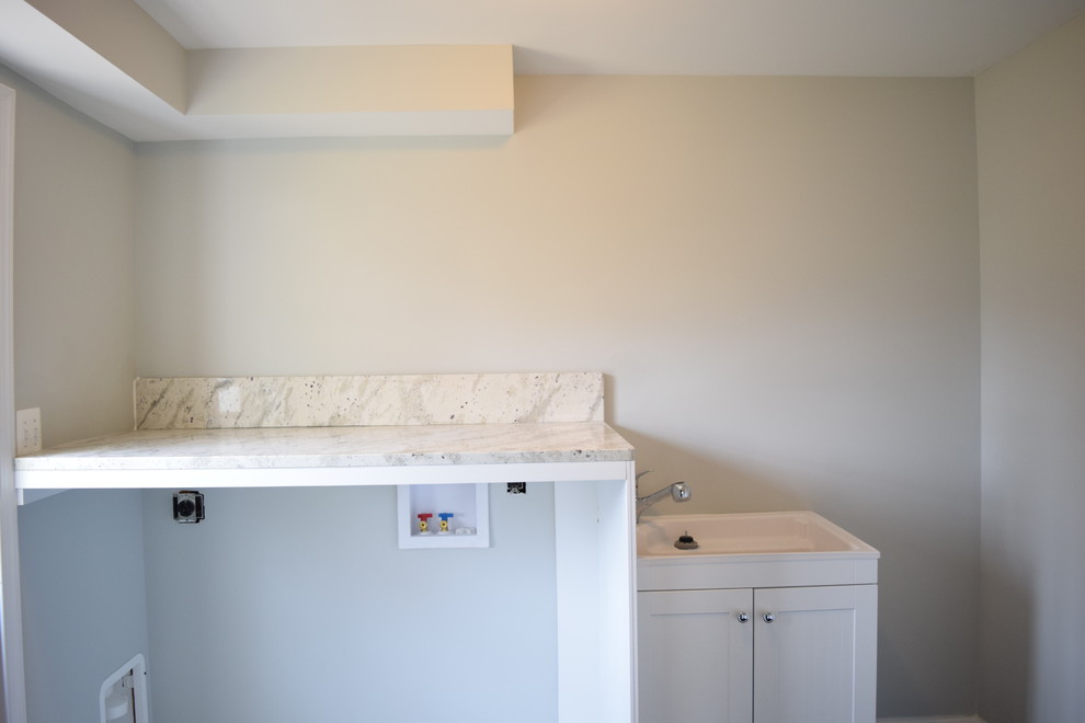 Photo of a mid-sized traditional single-wall utility room in Baltimore with a single-bowl sink, flat-panel cabinets, white cabinets, granite benchtops, grey walls, dark hardwood floors, a side-by-side washer and dryer and black floor.
