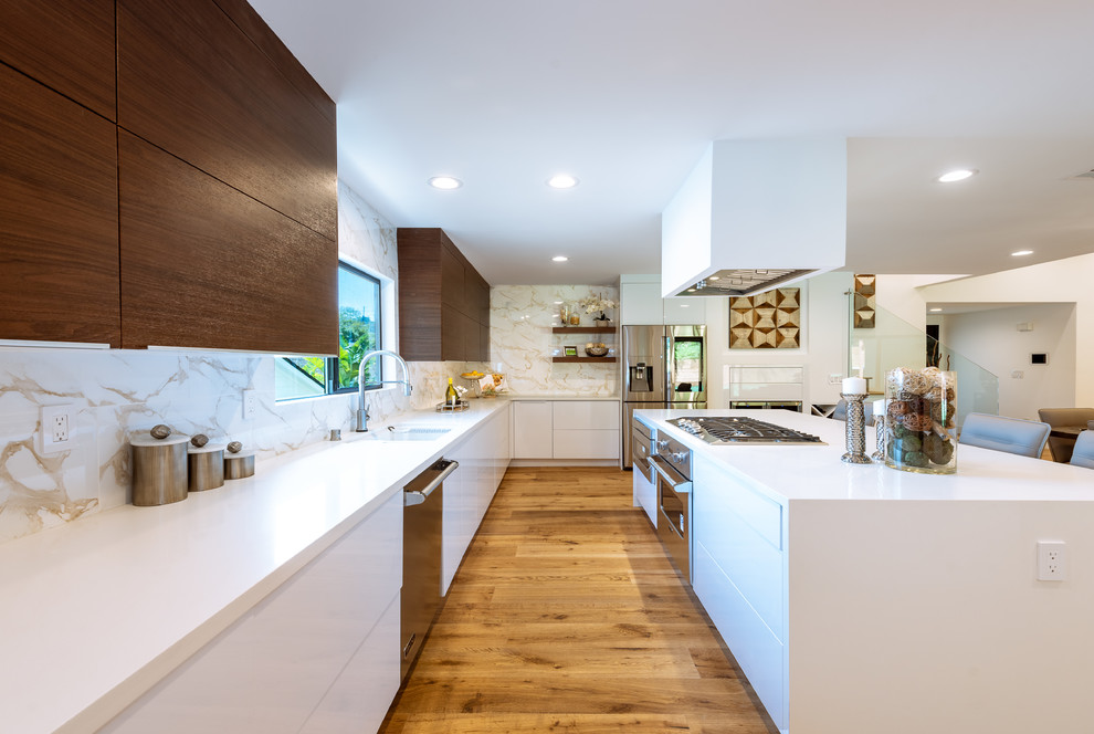 Photo of a large contemporary l-shaped eat-in kitchen in Los Angeles with an undermount sink, flat-panel cabinets, dark wood cabinets, white splashback, stainless steel appliances, medium hardwood floors, with island, brown floor, white benchtop, quartz benchtops and porcelain splashback.