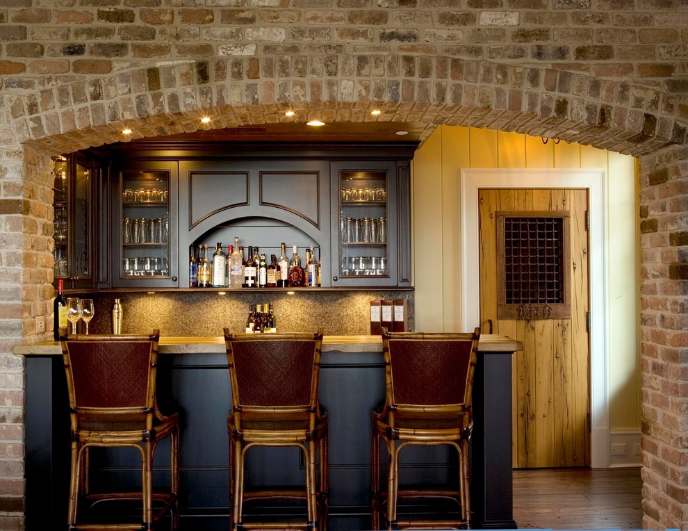 Inspiration for a mid-sized traditional galley seated home bar in Charleston with glass-front cabinets, black cabinets, brown splashback, dark hardwood floors, granite benchtops, mosaic tile splashback and brown floor.