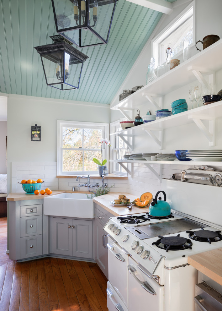 Small beach style galley separate kitchen in Los Angeles with a farmhouse sink, shaker cabinets, grey cabinets, wood benchtops, white splashback, ceramic splashback, white appliances, medium hardwood floors, no island, brown floor and beige benchtop.