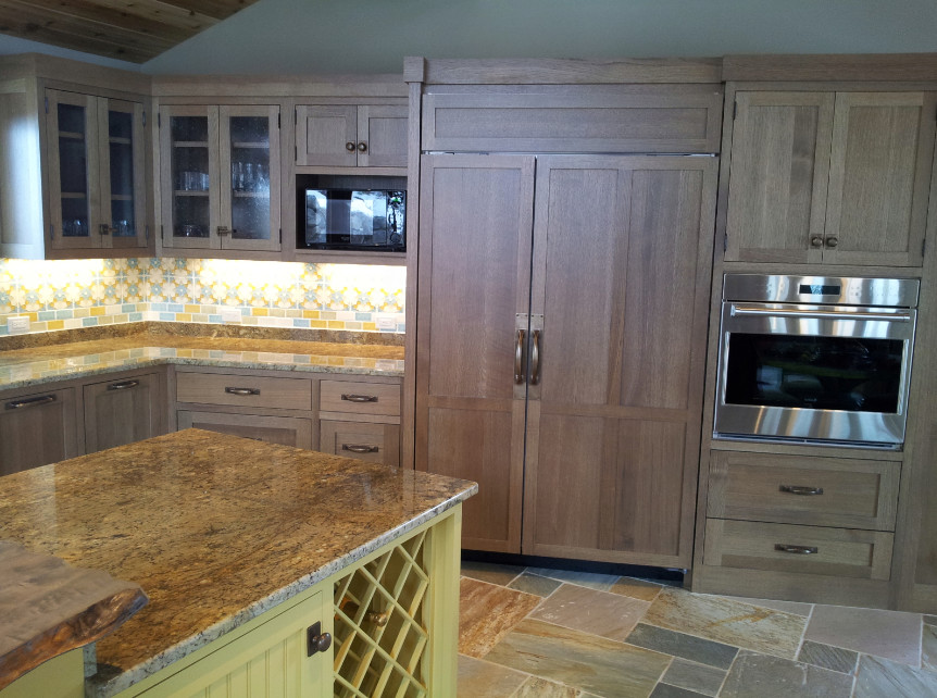 This is an example of a large arts and crafts u-shaped eat-in kitchen in Portland Maine with shaker cabinets, granite benchtops, mosaic tile splashback, stainless steel appliances, slate floors, with island, a farmhouse sink, light wood cabinets, multi-coloured splashback and multi-coloured floor.