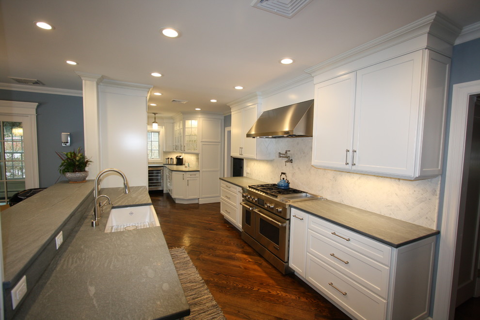 Photo of a large contemporary l-shaped kitchen in New York with a farmhouse sink, recessed-panel cabinets, white cabinets, soapstone benchtops, grey splashback, marble splashback and medium hardwood floors.