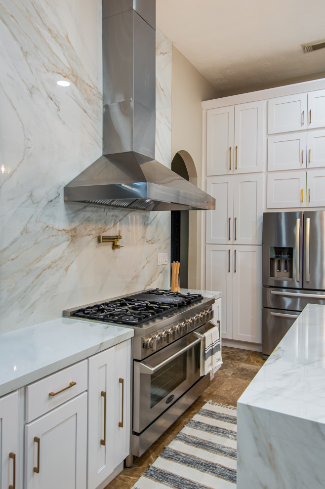 This is an example of a large modern l-shaped eat-in kitchen in Houston with an undermount sink, shaker cabinets, white cabinets, solid surface benchtops, white splashback, porcelain splashback, stainless steel appliances, marble floors, with island, beige floor and white benchtop.