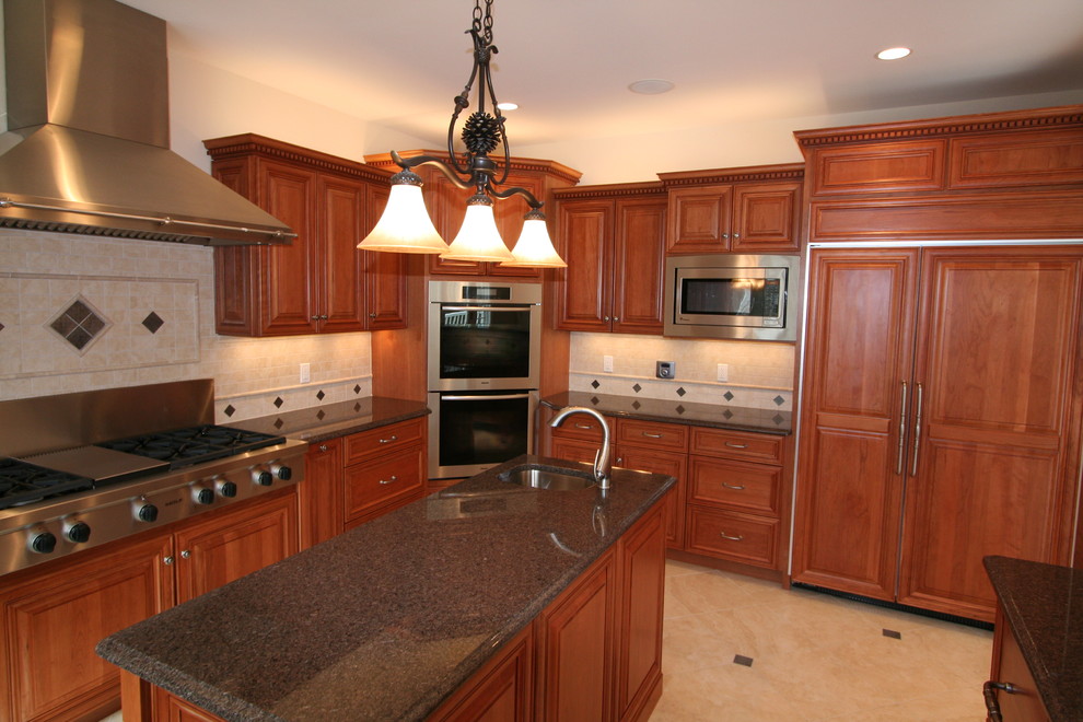 This is an example of a large traditional kitchen in New York with an undermount sink, raised-panel cabinets, medium wood cabinets, granite benchtops, beige splashback, porcelain splashback, stainless steel appliances, porcelain floors, with island, beige floor and black benchtop.