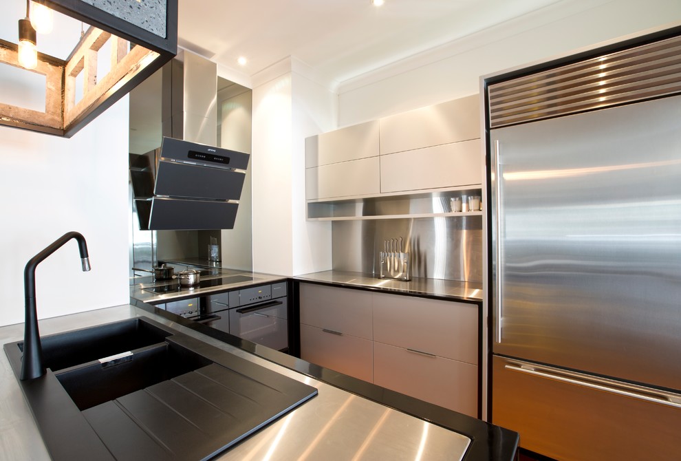 Inspiration for a small industrial u-shaped separate kitchen in Brisbane with a double-bowl sink, flat-panel cabinets, grey cabinets, stainless steel benchtops, grey splashback, metal splashback, black appliances, medium hardwood floors and with island.