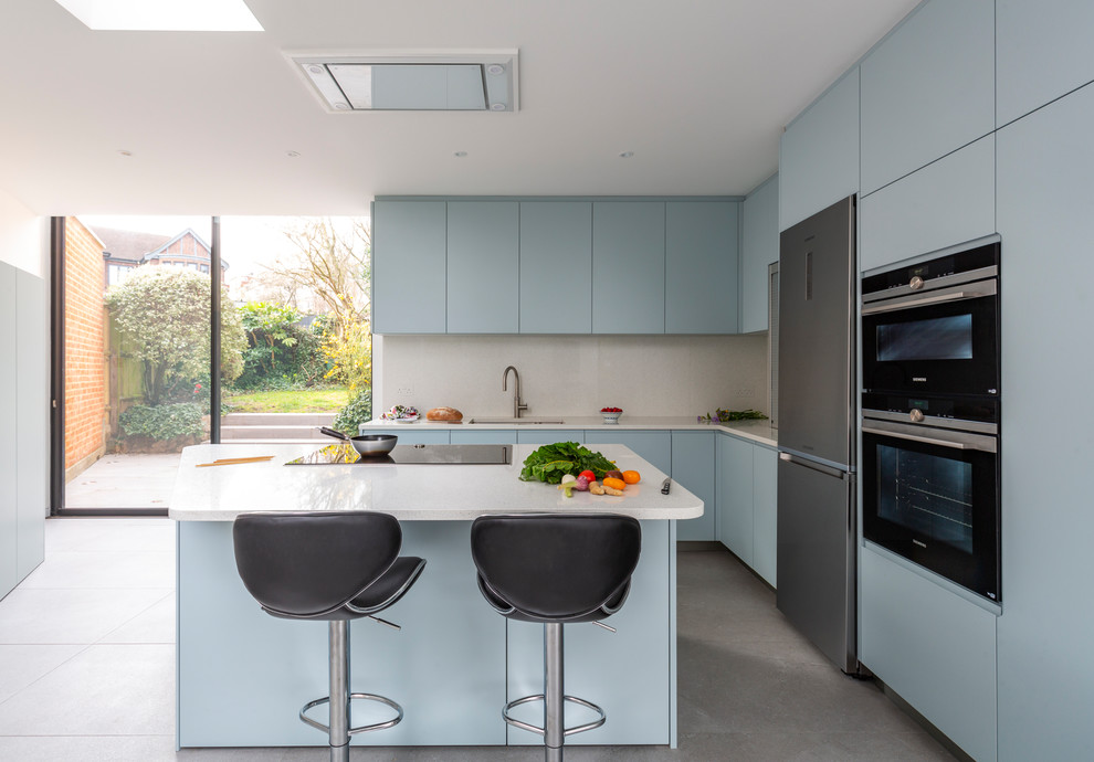 Photo of a mid-sized contemporary open plan kitchen in London with flat-panel cabinets, blue cabinets, black appliances, with island and white benchtop.