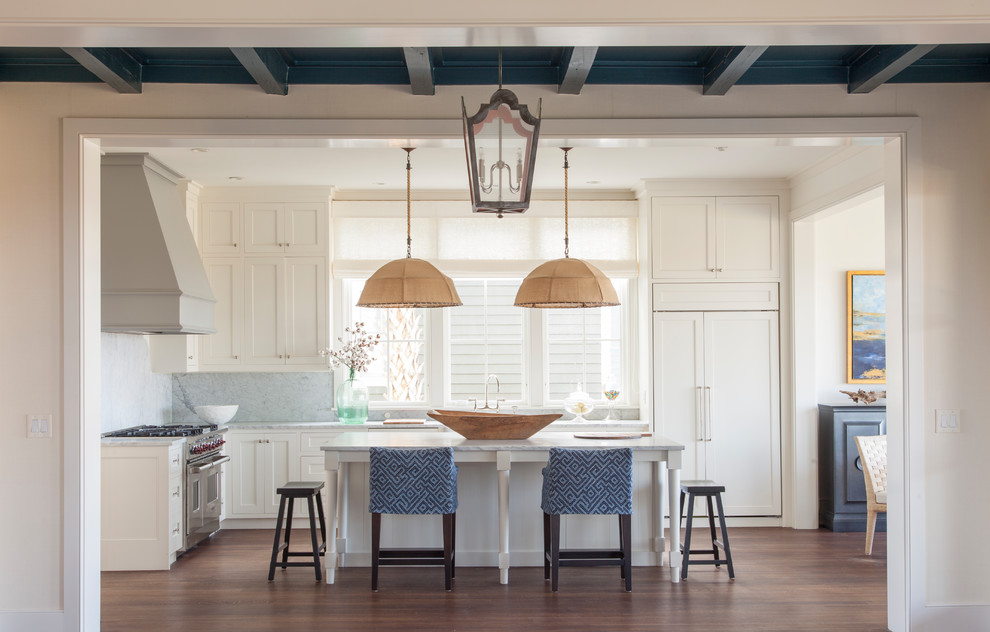 Design ideas for a beach style l-shaped kitchen in Charleston with white cabinets, marble benchtops, white splashback, stainless steel appliances, medium hardwood floors, with island, shaker cabinets and stone slab splashback.