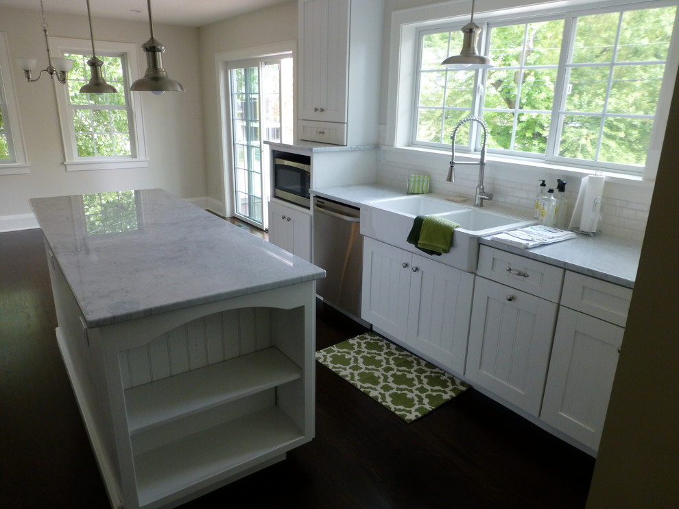 Large country galley eat-in kitchen in Minneapolis with a farmhouse sink, beaded inset cabinets, white cabinets, marble benchtops, white splashback, ceramic splashback, stainless steel appliances, dark hardwood floors, with island and brown floor.