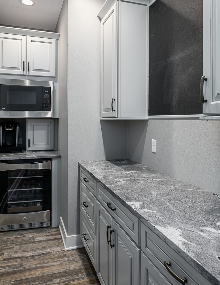 Inspiration for a mid-sized transitional single-wall ceramic tile and multicolored floor kitchen pantry remodel with a farmhouse sink, raised-panel cabinets, gray cabinets, granite countertops, white backsplash, subway tile backsplash, black appliances, an island and white countertops