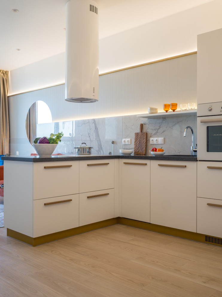 This is an example of a mid-sized contemporary l-shaped open plan kitchen in Other with a drop-in sink, flat-panel cabinets, white cabinets, solid surface benchtops, grey splashback, porcelain splashback, white appliances, porcelain floors, beige floor, grey benchtop and a peninsula.