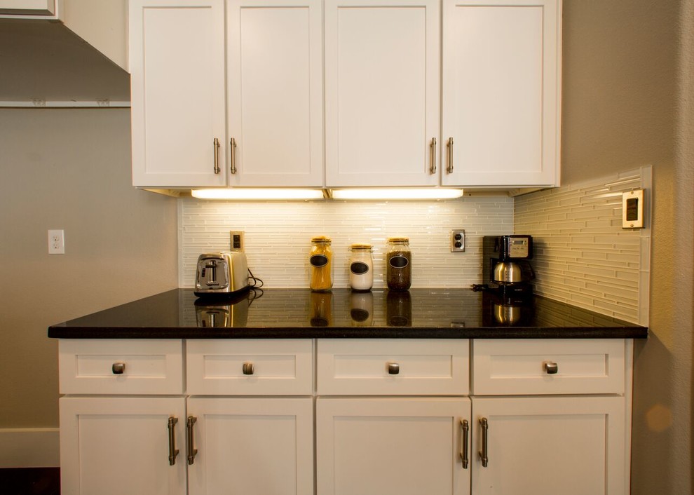 Home design - transitional porcelain tile home design idea in Austin with an undermount sink, shaker cabinets, white cabinets, granite countertops, white backsplash, glass sheet backsplash, stainless steel appliances and an island