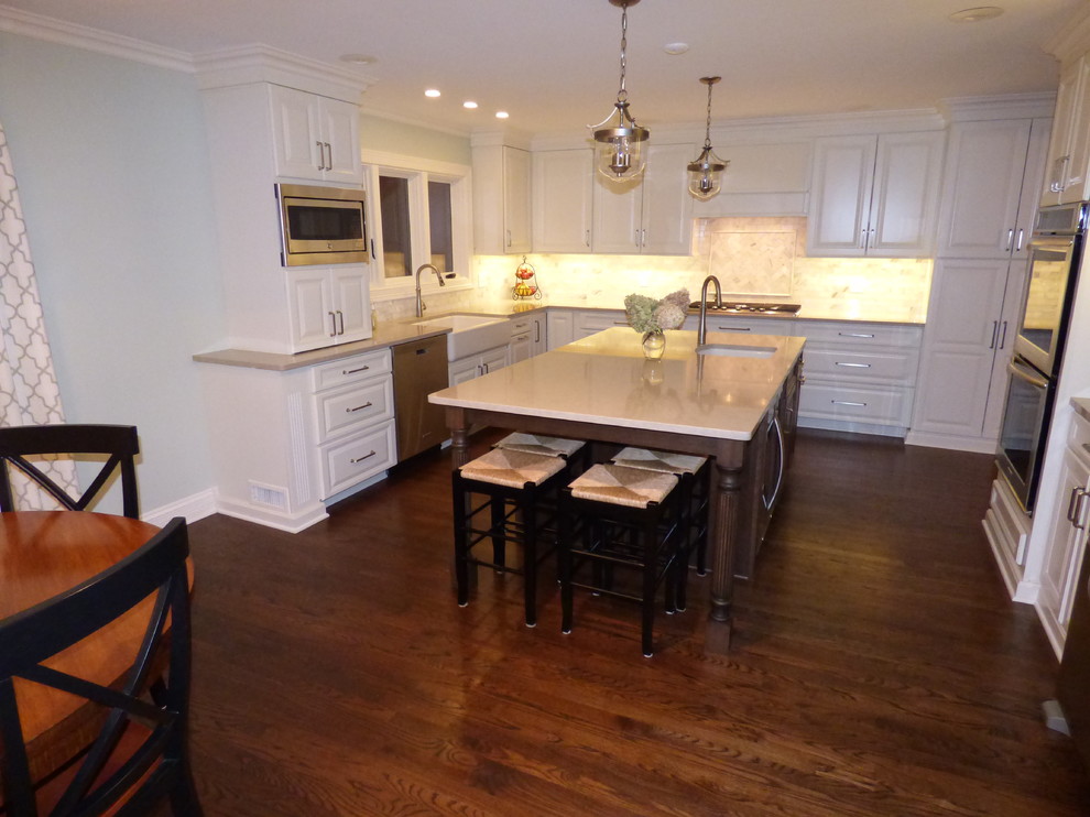 Inspiration for a large transitional u-shaped dark wood floor eat-in kitchen remodel in Chicago with a farmhouse sink, raised-panel cabinets, white cabinets, quartz countertops, gray backsplash, stone tile backsplash, stainless steel appliances and an island