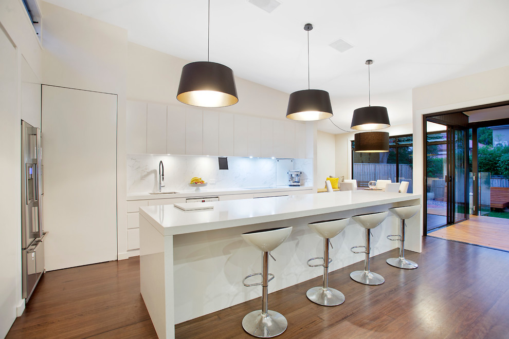 Contemporary kitchen in Sydney with flat-panel cabinets, white cabinets, white splashback, stainless steel appliances, medium hardwood floors and with island.