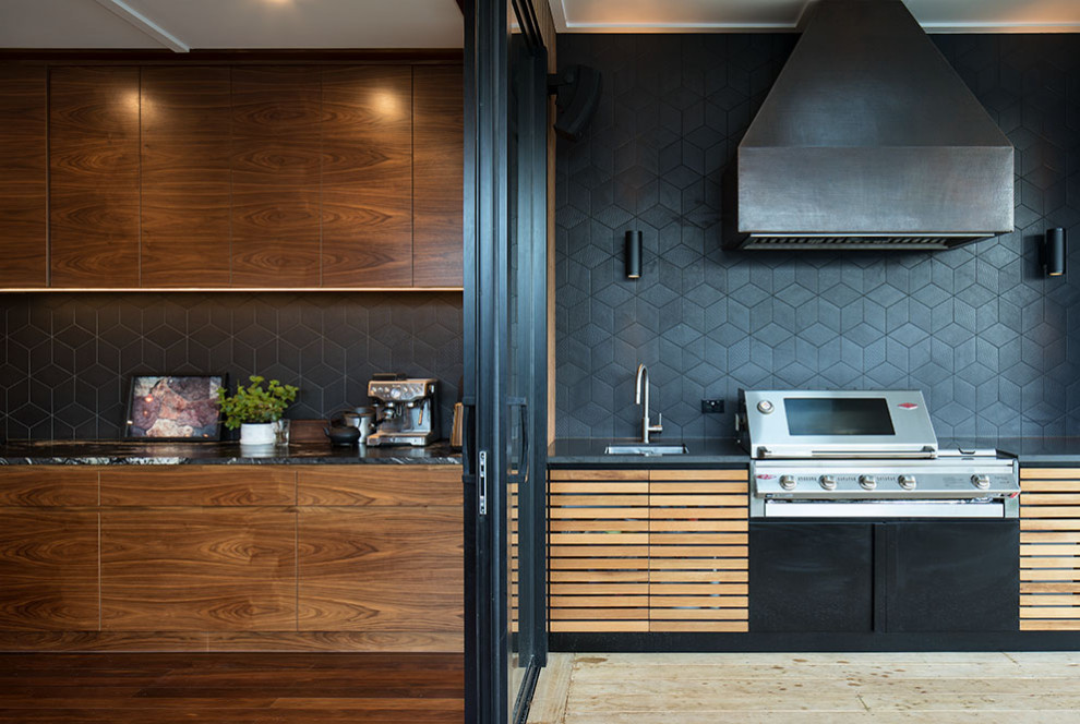 This is an example of a large midcentury l-shaped eat-in kitchen in Auckland with a double-bowl sink, raised-panel cabinets, medium wood cabinets, granite benchtops, black splashback, ceramic splashback, black appliances, with island and black benchtop.