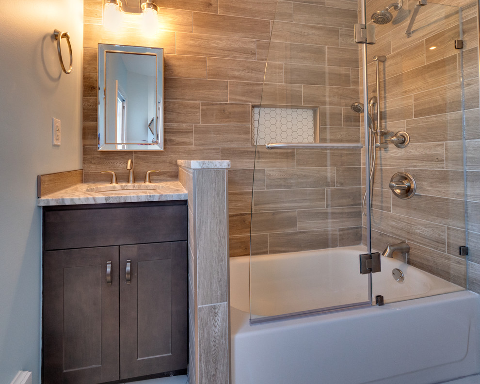 This is an example of a mid-sized transitional kids bathroom in Philadelphia with recessed-panel cabinets, medium wood cabinets, a corner tub, a shower/bathtub combo, a two-piece toilet, brown tile, porcelain tile, brown walls, porcelain floors, an undermount sink, limestone benchtops, grey floor, an open shower and grey benchtops.