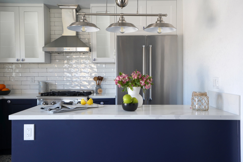 Photo of a mid-sized beach style l-shaped eat-in kitchen in Orange County with a farmhouse sink, shaker cabinets, blue cabinets, quartz benchtops, white splashback, ceramic splashback, white appliances, cement tiles, a peninsula, blue floor and white benchtop.