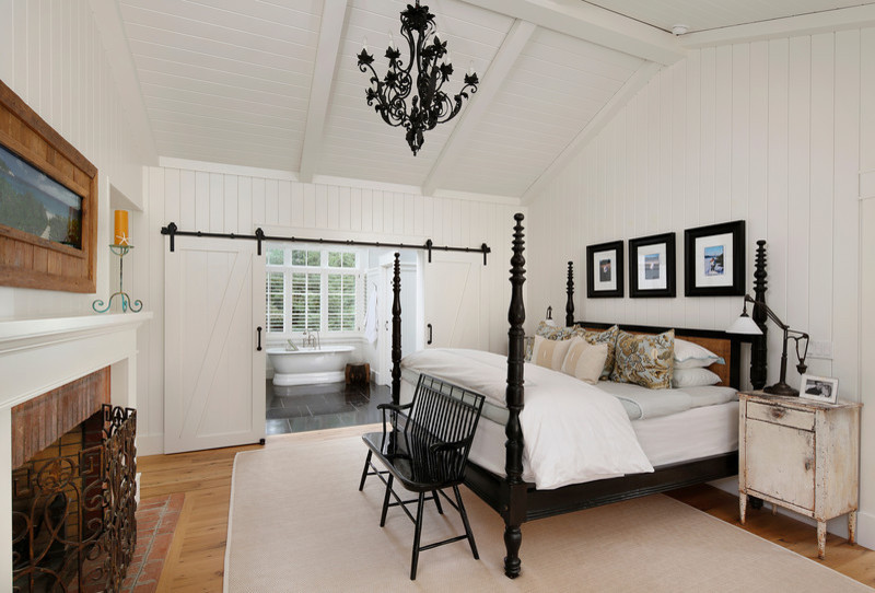 This is an example of a mid-sized country guest bedroom in San Francisco with white walls, light hardwood floors, a standard fireplace, a brick fireplace surround and brown floor.