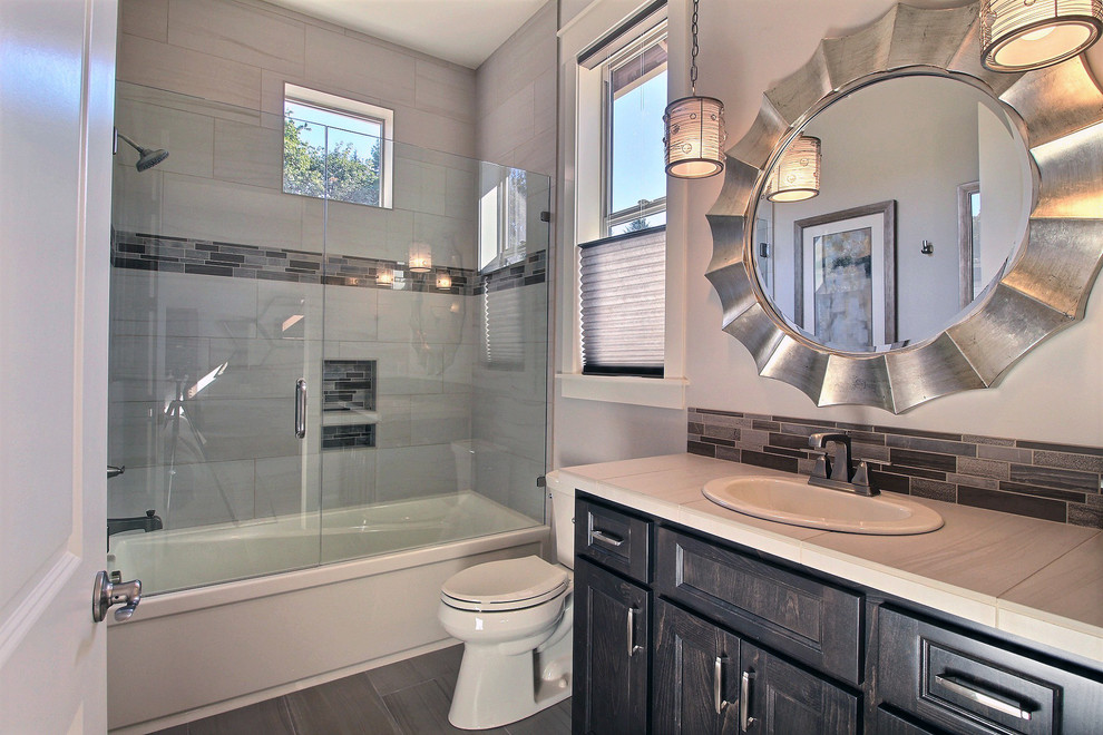 This is an example of a large transitional 3/4 bathroom in Portland with recessed-panel cabinets, dark wood cabinets, a drop-in tub, a curbless shower, a two-piece toilet, gray tile, ceramic tile, beige walls, porcelain floors, an undermount sink, tile benchtops, grey floor and an open shower.