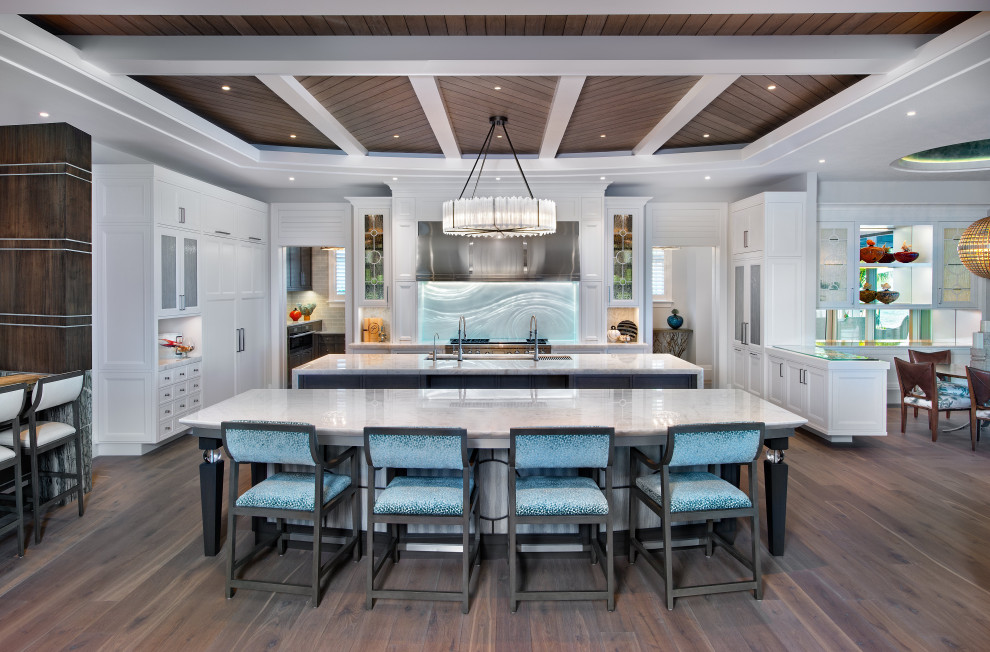 This is an example of a mediterranean u-shaped open plan kitchen in Miami with an undermount sink, shaker cabinets, white cabinets, blue splashback, stainless steel appliances, multiple islands, brown floor, white benchtop, wood and medium hardwood floors.