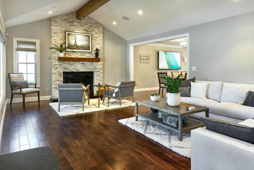 This is an example of a large transitional open concept family room in San Francisco with grey walls, dark hardwood floors, a standard fireplace, brown floor and exposed beam.