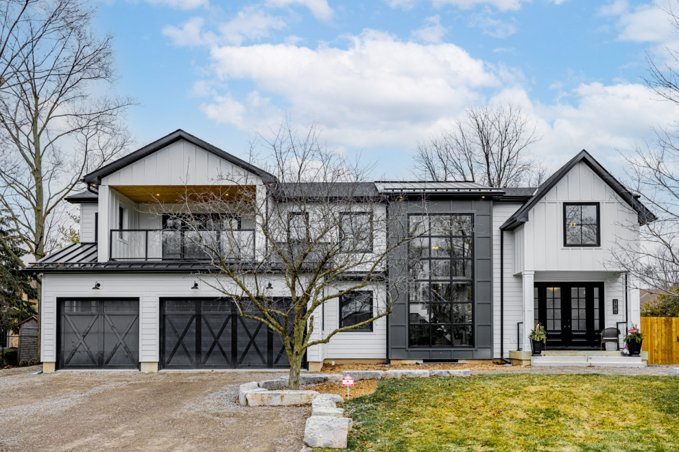 Large and white farmhouse two floor concrete detached house in Toronto with a pitched roof, a black roof, shiplap cladding and a shingle roof.