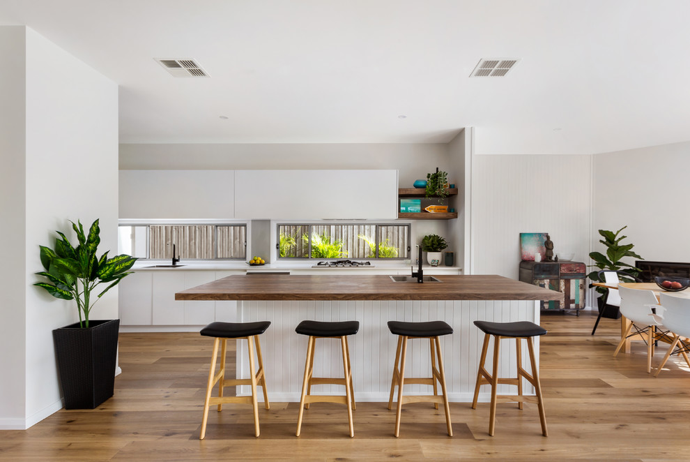 This is an example of a contemporary eat-in kitchen in Sydney with a drop-in sink, flat-panel cabinets, white cabinets, window splashback, medium hardwood floors, multiple islands, brown floor, wood benchtops, stainless steel appliances and brown benchtop.