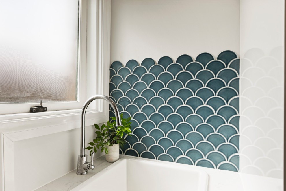 Design ideas for a small traditional galley dedicated laundry room in Sydney with a drop-in sink, flat-panel cabinets, blue splashback, mosaic tile splashback, white walls, a stacked washer and dryer and white benchtop.