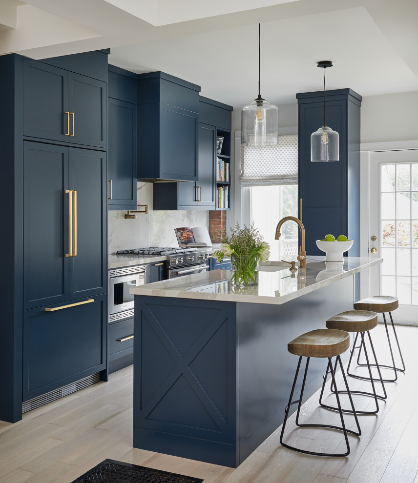 Photo of a transitional galley kitchen in Toronto with a farmhouse sink, shaker cabinets, blue cabinets, white splashback, stainless steel appliances, light hardwood floors, with island, beige floor and white benchtop.