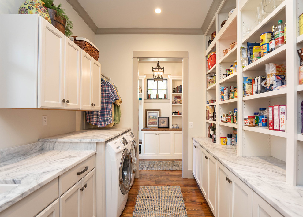 Photo of a country galley utility room in Atlanta with recessed-panel cabinets, white cabinets, white walls, medium hardwood floors, a side-by-side washer and dryer, brown floor and grey benchtop.