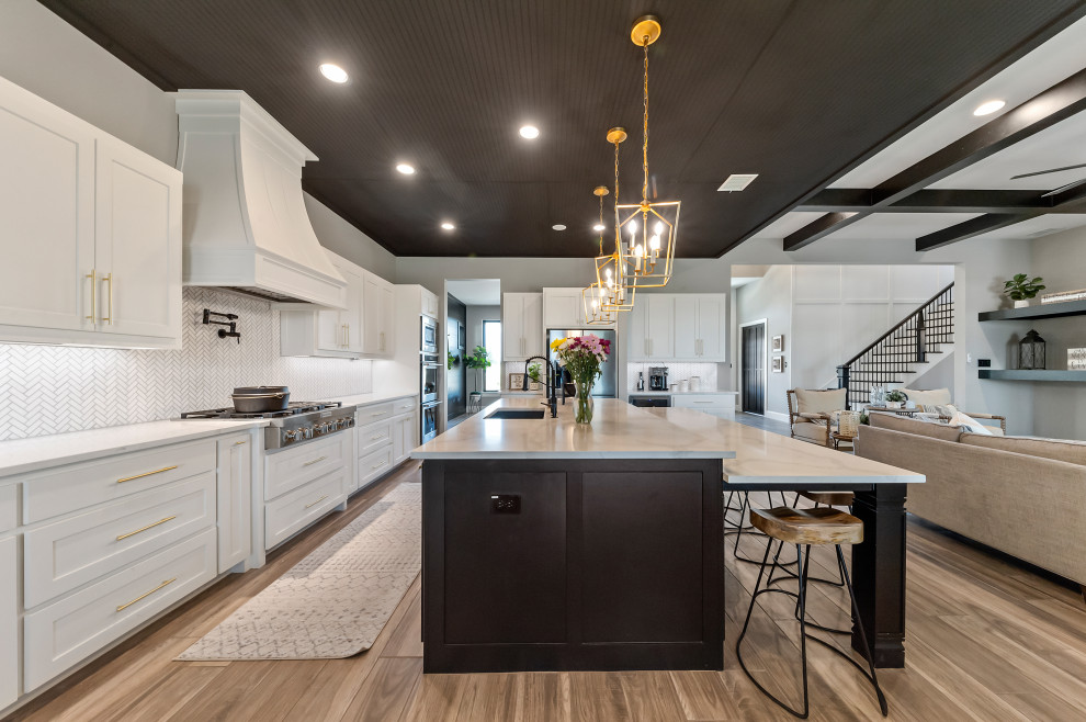 Large country l-shaped open plan kitchen in Dallas with an undermount sink, recessed-panel cabinets, white cabinets, quartzite benchtops, white splashback, mosaic tile splashback, stainless steel appliances, medium hardwood floors, multiple islands, brown floor, white benchtop and timber.