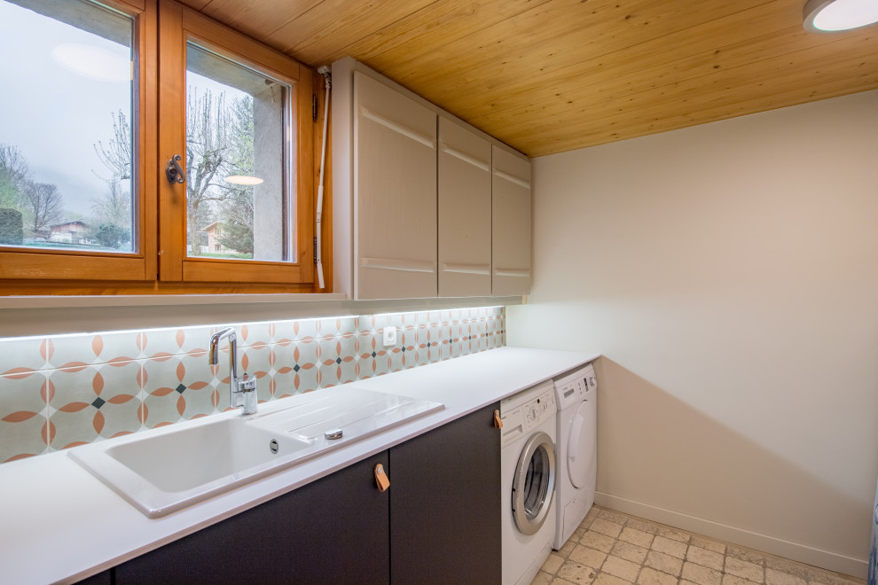 リヨンにあるお手頃価格の中くらいな北欧スタイルのおしゃれなランドリールーム (I型、ドロップインシンク、ラミネートカウンター、マルチカラーのキッチンパネル、ボーダータイルのキッチンパネル、ベージュの壁、トラバーチンの床、左右配置の洗濯機・乾燥機、ベージュの床、白いキッチンカウンター) の写真