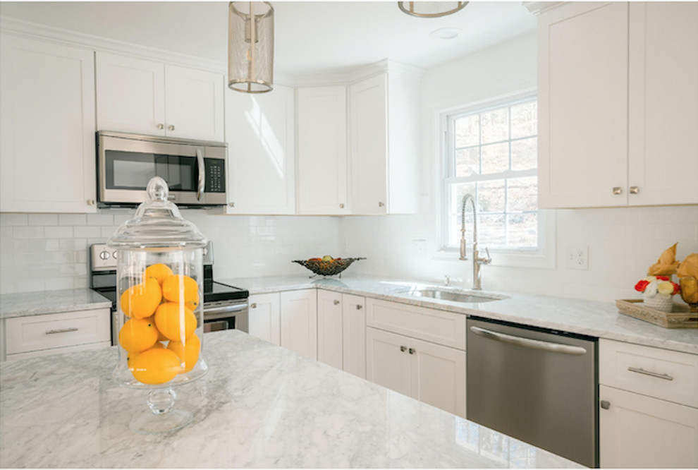 Mid-sized transitional l-shaped open plan kitchen in Bridgeport with an undermount sink, shaker cabinets, white cabinets, marble benchtops, white splashback, subway tile splashback, stainless steel appliances, medium hardwood floors, with island and brown floor.