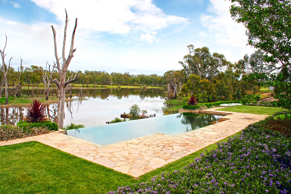 Design ideas for a large country infinity pool in Melbourne with natural stone pavers.