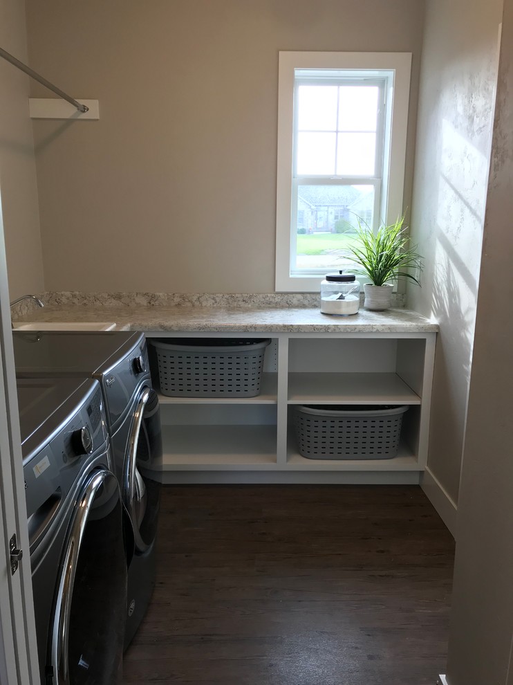 Large contemporary l-shaped dedicated laundry room in Other with a drop-in sink, open cabinets, white cabinets, laminate benchtops, grey walls, vinyl floors, a side-by-side washer and dryer, brown floor and grey benchtop.