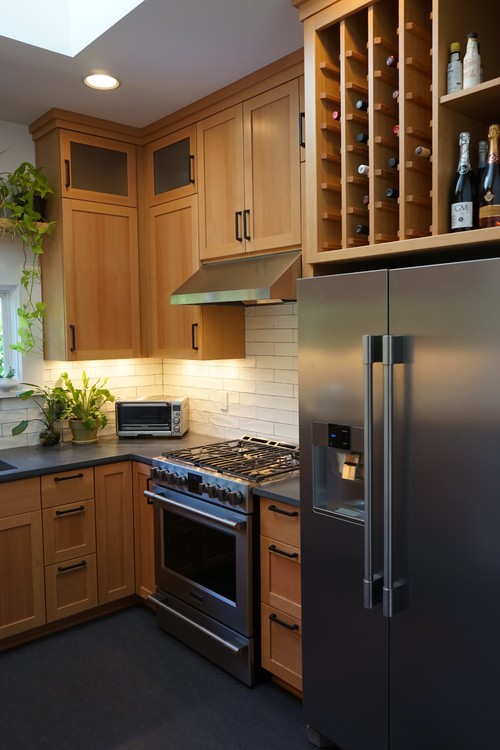 Compact kitchen with light wood shaker cabinets, wine rack, stainless fridge and range, and under-cabinet lighting