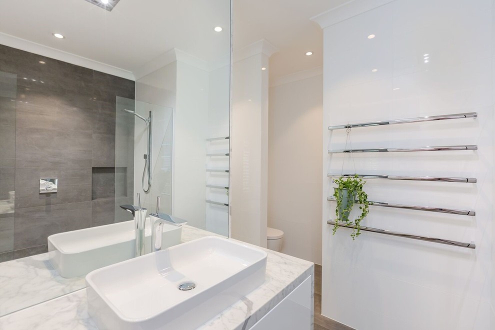 Inspiration for a large contemporary 3/4 bathroom in Adelaide with an open shower, white tile, ceramic tile, white walls, porcelain floors, brown floor, an open shower, flat-panel cabinets, white cabinets, an undermount tub, a one-piece toilet, a vessel sink, marble benchtops and white benchtops.