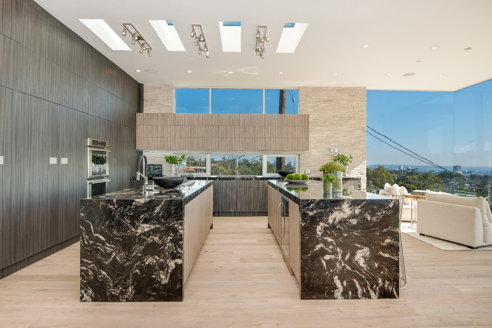 Expansive contemporary l-shaped open plan kitchen in Los Angeles with an undermount sink, flat-panel cabinets, medium wood cabinets, marble benchtops, brown splashback, stone tile splashback, panelled appliances, light hardwood floors, multiple islands and beige floor.