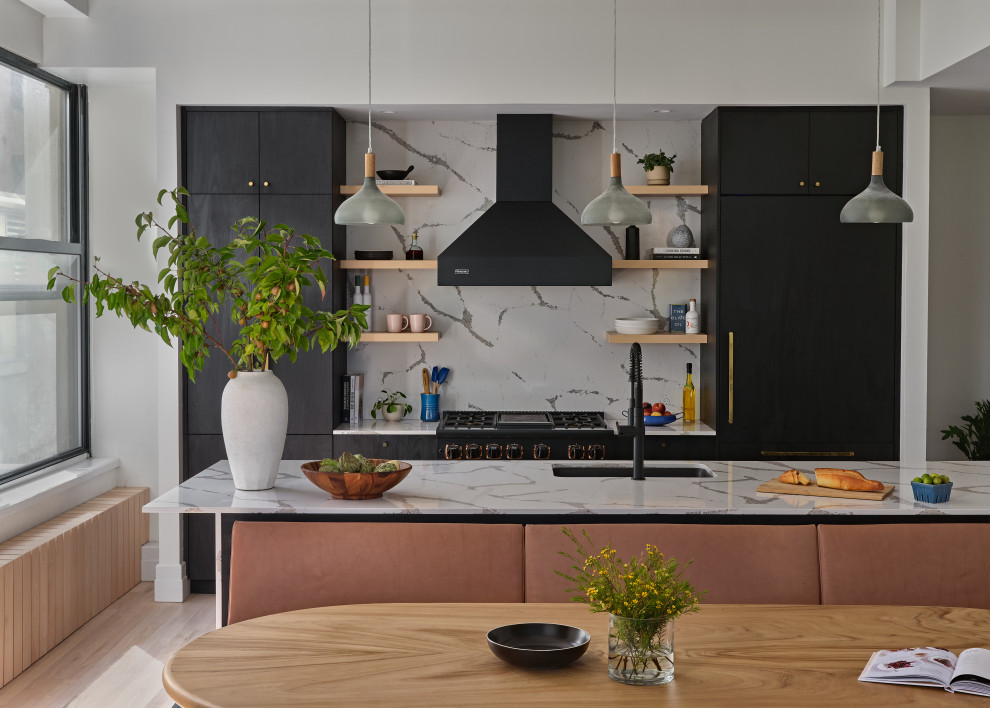 Photo of a contemporary galley kitchen in New York with an undermount sink, flat-panel cabinets, black cabinets, white splashback, stone slab splashback, black appliances, light hardwood floors, with island, beige floor and white benchtop.