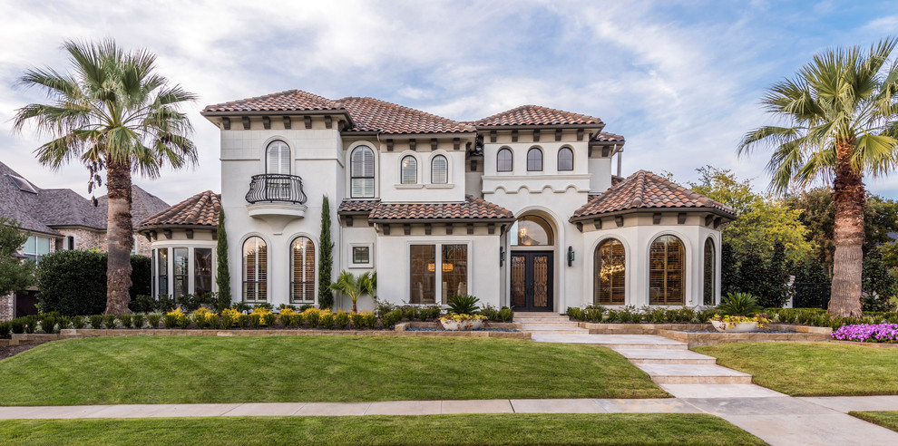 Inspiration for a large mediterranean two-storey stucco beige house exterior in Dallas with a hip roof and a tile roof.