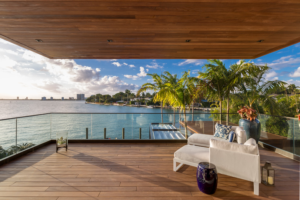 Inspiration for a contemporary balcony in Miami with a roof extension and glass railing.