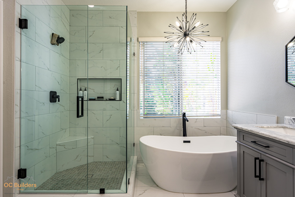 This is an example of a mid-sized midcentury master bathroom in Orange County with shaker cabinets, grey cabinets, a freestanding tub, a corner shower, a one-piece toilet, white tile, marble, beige walls, ceramic floors, an undermount sink, quartzite benchtops, white floor, a hinged shower door, grey benchtops, a shower seat, a double vanity and a built-in vanity.