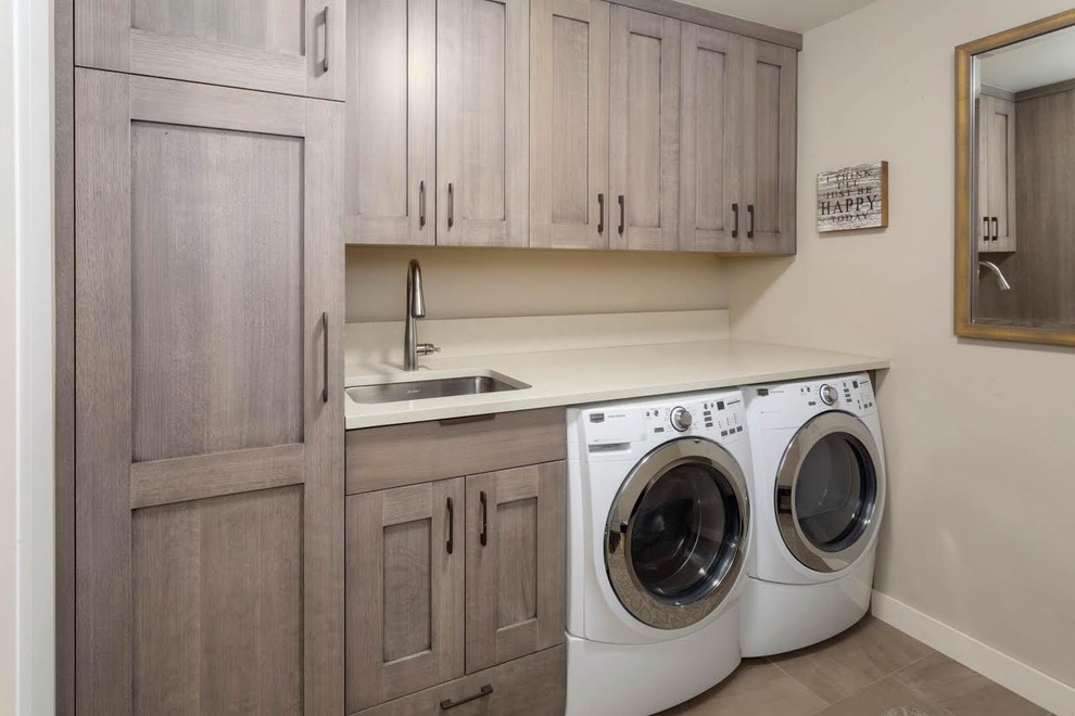 Example of a mid-sized transitional single-wall porcelain tile and brown floor dedicated laundry room design in Denver with an undermount sink, shaker cabinets, medium tone wood cabinets, quartz countertops, beige walls, a side-by-side washer/dryer and white countertops