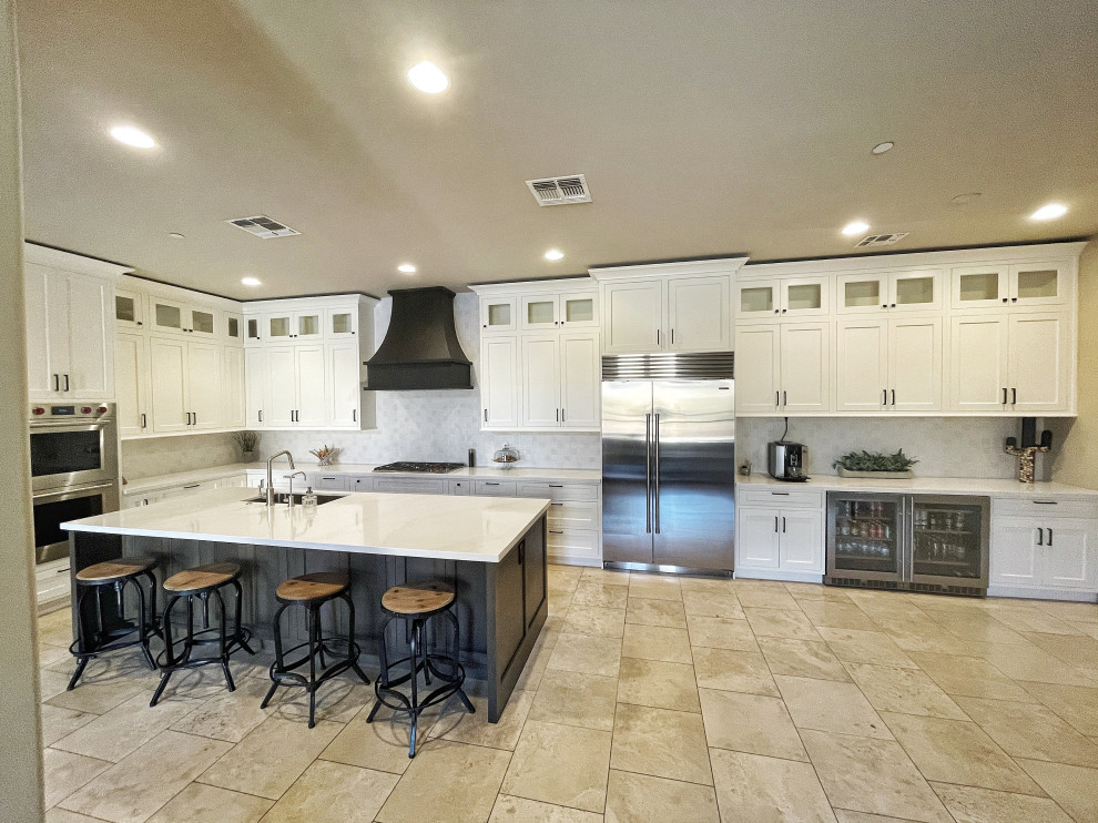 This is an example of an expansive classic l-shaped kitchen/diner in Phoenix with a submerged sink, shaker cabinets, white cabinets, engineered stone countertops, white splashback, ceramic splashback, stainless steel appliances, travertine flooring, an island, beige floors, white worktops and a vaulted ceiling.